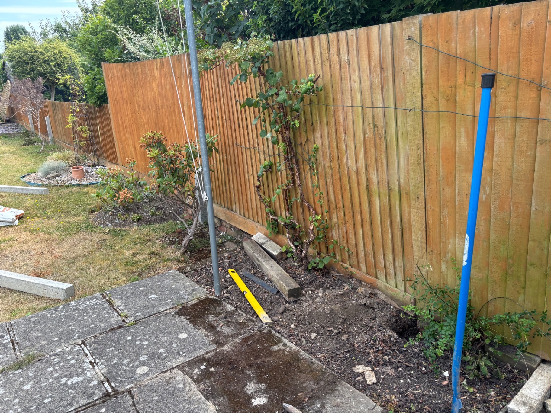 Leaning closeboard fence excavated at the base, ready for a concrete spur repair